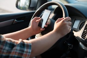 Texting and talking while driving, hands of young man on steering wheel